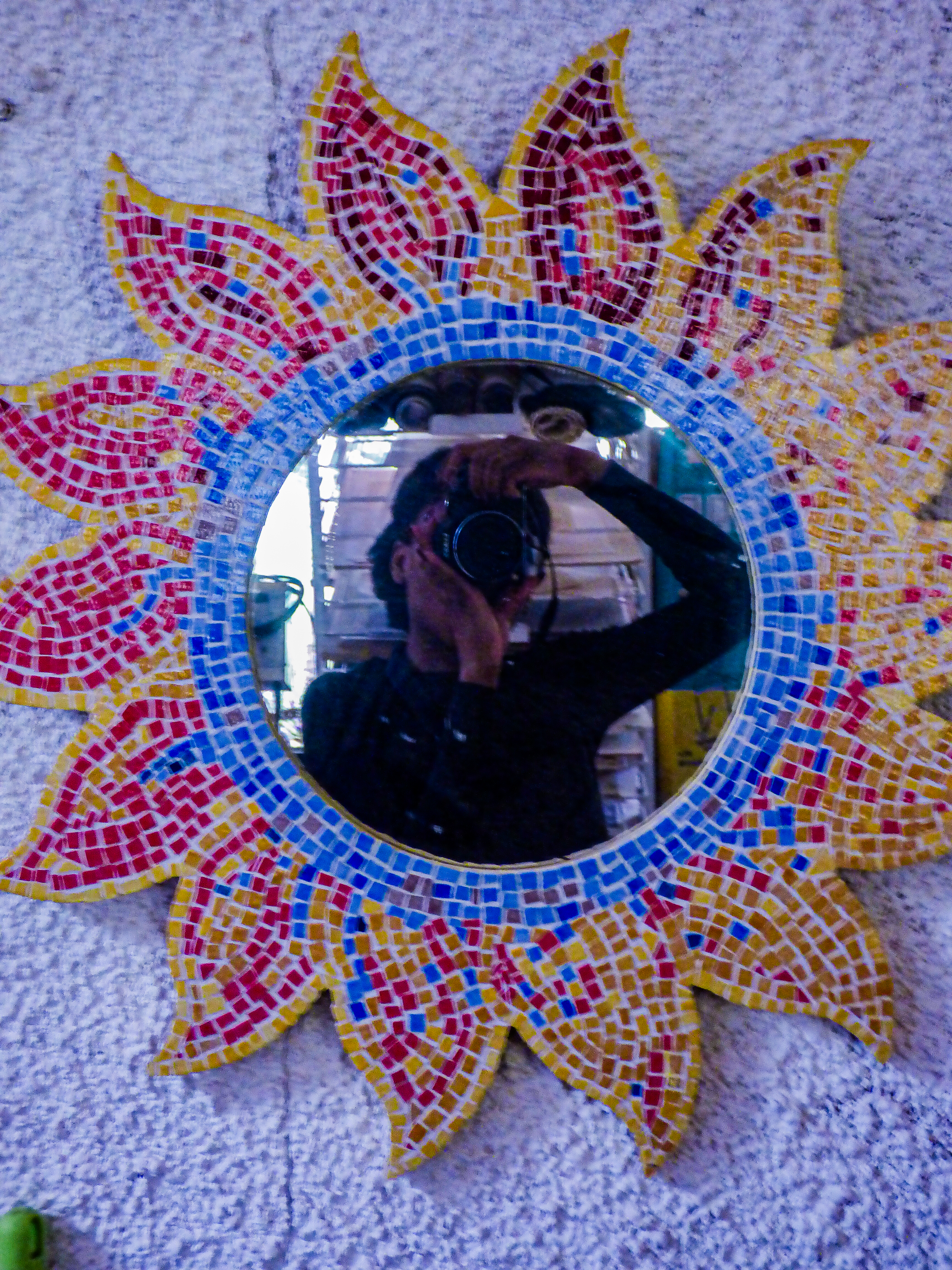 Photo d'un miroir en forme de soleil, dans lequel se reflete la photographe portant l'appareil